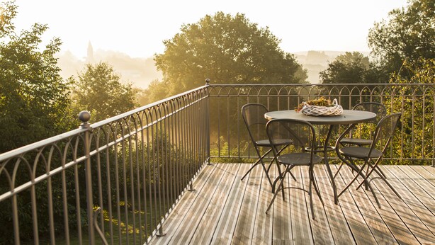 A wooden deck with a metal railing, a round table with two chairs, and a basket on the table. - B&B Le Verger du Pierroy (Léglise)