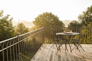 Eine Holzterrasse mit Metallgeländer, einem runden Tisch und zwei Stühlen, sowie einem Korb auf dem Tisch.