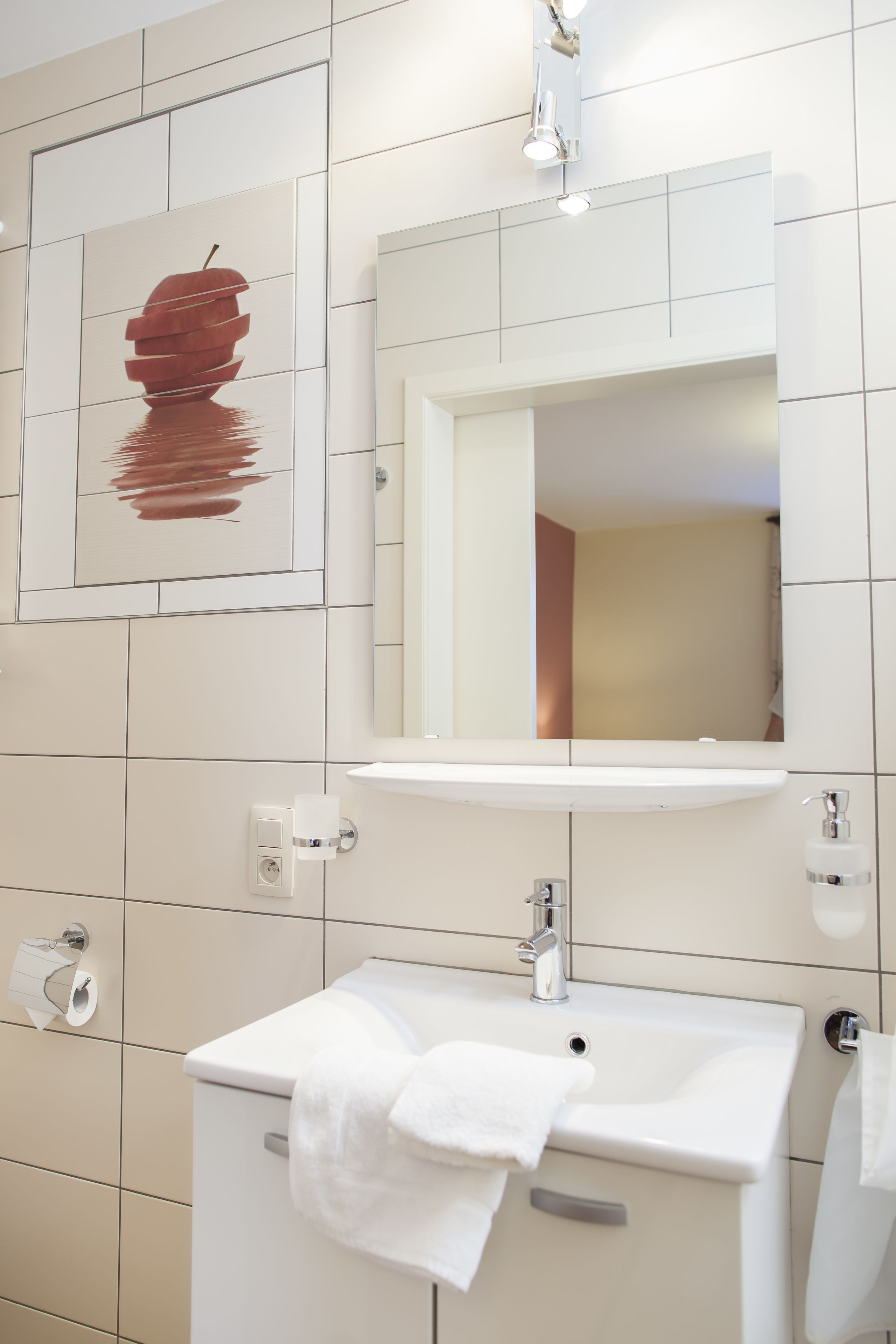 A modern bathroom with a white sink, a mirror above it, and a toilet with a roll of toilet paper.