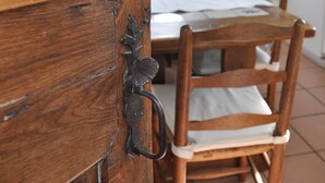 A wooden dining table with chairs, a window with curtains, and a kitchen area with cabinets. - B&B Le Verger du Pierroy (Léglise)