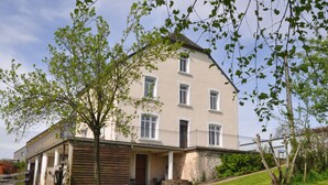 A two-story building with a balcony, a covered porch, and a stone foundation. - B&B Le Verger du Pierroy (Léglise)