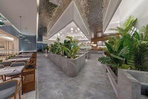 Un intérieur moderne avec un espace salon central, plusieurs tables et des plantes en pot.
