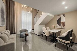 Una habitación de hotel moderna con sofá, mesa de comedor, sillas, una mesita auxiliar y una escalera.