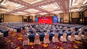 A large conference room with rows of tables and chairs, a stage with a red backdrop, and ornate chandeliers. - Zhangjiakou International Hotel (Building B ) (Zhangjiakou)