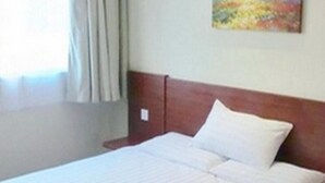 A hotel room with a bed, a nightstand, a painting on the wall, and a window with curtains.