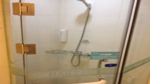 A glass-enclosed shower stall with a towel hanging on the door, a glass shelf, and a sign with text.