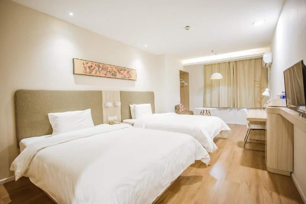 A hotel room with two beds, a desk, a chair, a mirror, and a painting on the wall.