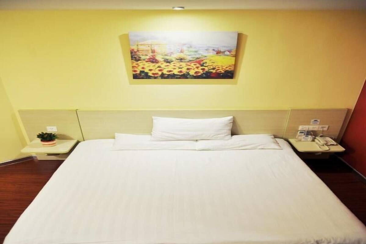 A hotel room with a bed, a bedside table with a phone, a small plant, and a painting on the wall.