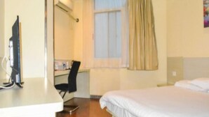 A hotel room with a bed, a desk with a chair, a television, and a window with curtains.