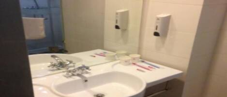 A bathroom with a white sink, mirror, and two towel dispensers.