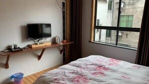 Une chambre d’hôtel avec un lit, un téléviseur posé sur une étagère en bois, une fenêtre donnant sur des immeubles et une petite table avec une bouilloire.