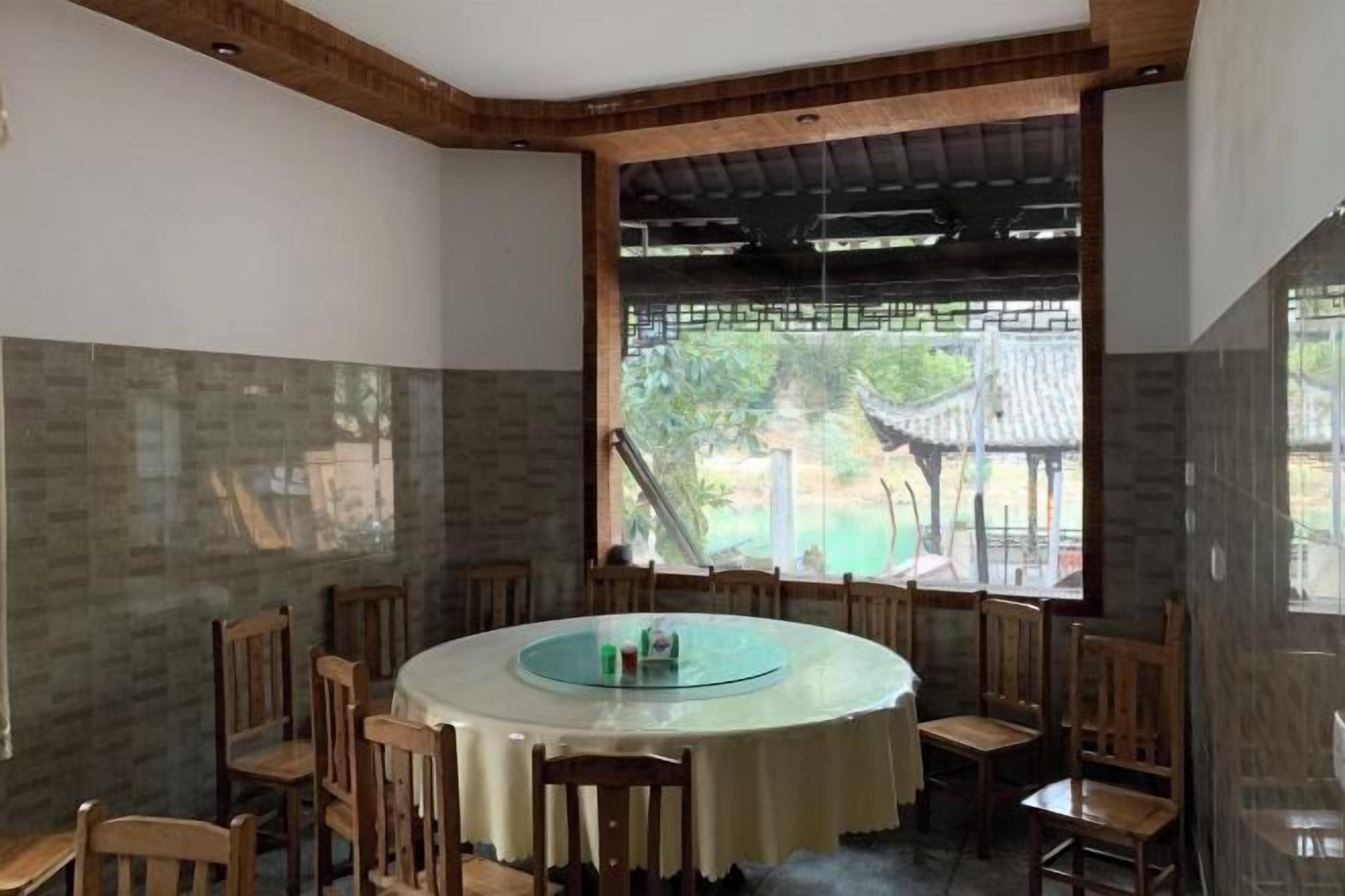 A round dining table with a glass top surrounded by wooden chairs, set against a wall with a tiled pattern.