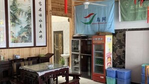 Un restaurant chinois traditionnel, avec des meubles en bois, une table à plateau en verre, un réfrigérateur et une banderole bleue sur laquelle figure l’adresse d’un site web.