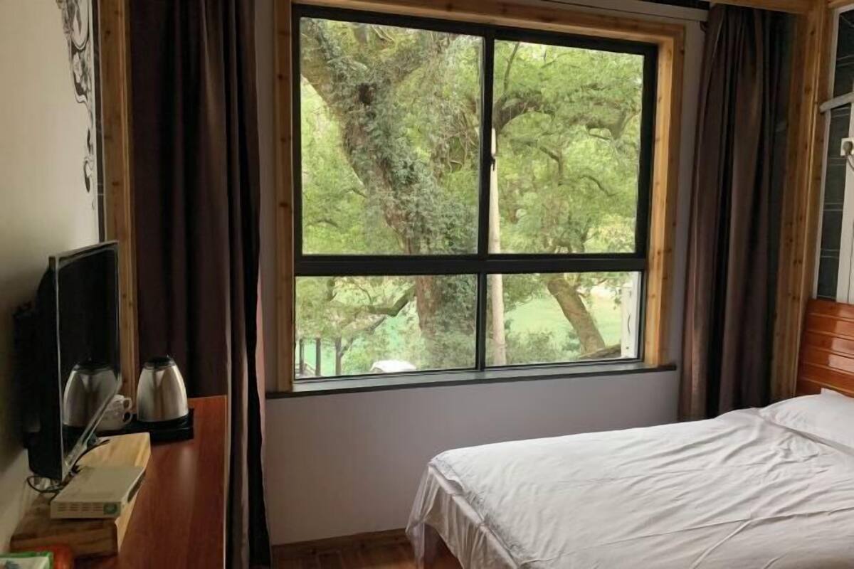 Ein Schlafzimmer mit großem Fenster, einem Bett, einem Nachttisch mit Lampe und einem Fernseher.