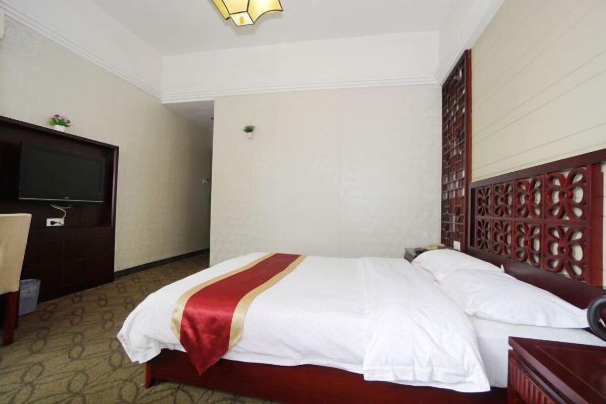 A hotel room with a bed, a TV, a desk, and a decorative wall panel.