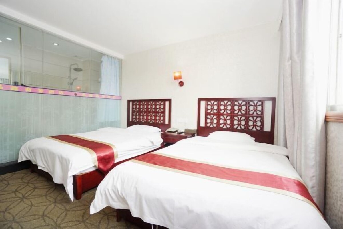 A hotel room with two beds, a mirror, a nightstand, and a small window.
