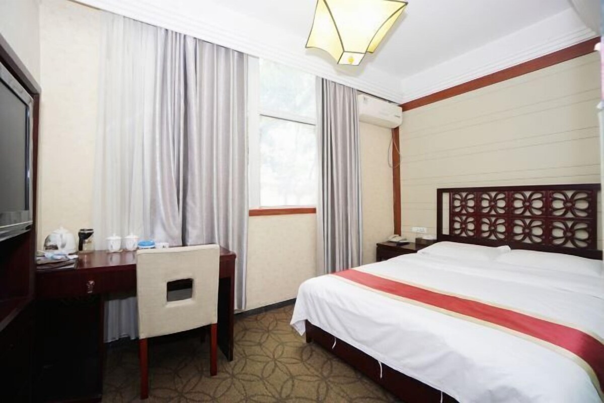 A hotel room with a bed, a desk, a chair, a TV, and curtains.
