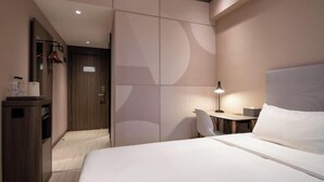 A hotel room with a bed, bedside table, lamp, and a desk with a chair.