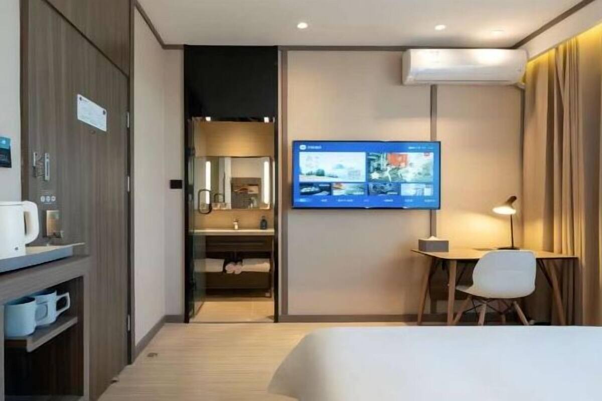 Ein Hotelzimmer mit Bett, Schreibtisch, Fernseher und einem durchgehenden Türrahmen einsehbaren Badezimmer.