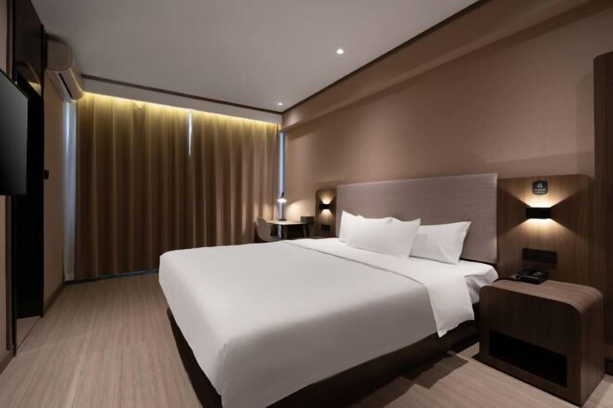 Ein modernes Hotelzimmer mit einem großen Bett, einem Nachttisch und einem an der Wand befestigten Fernseher.