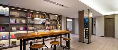 A modern library with bookshelves, a wooden table, and bar stools.