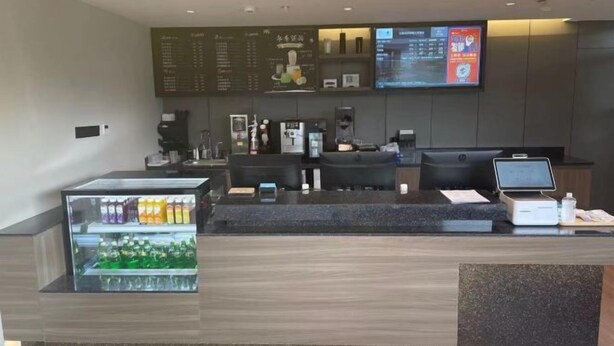 A reception desk with a digital screen, a coffee machine, and a beverage dispenser.