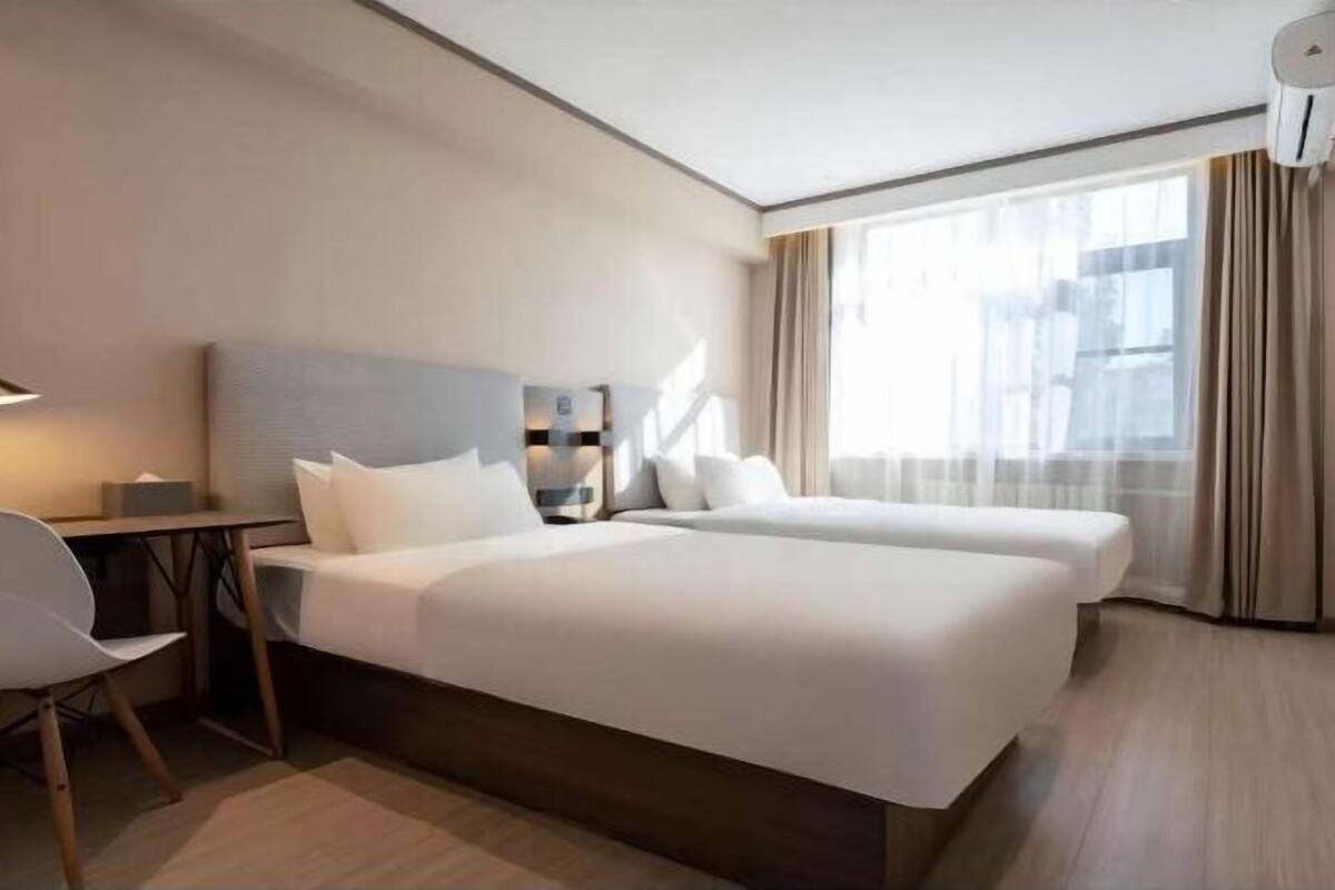 Ein modernes Hotelzimmer mit zwei Betten, einem Schreibtisch und einem Stuhl.
