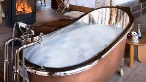 A bathroom with a freestanding bathtub, a wood-burning stove, and a bed with a canopy.