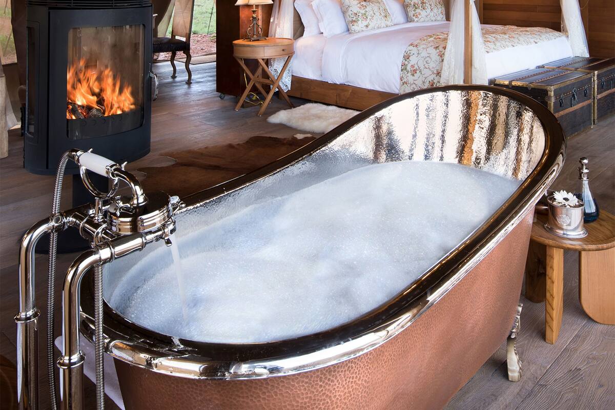 A bathroom with a freestanding bathtub, a wood-burning stove, and a bed with a canopy.