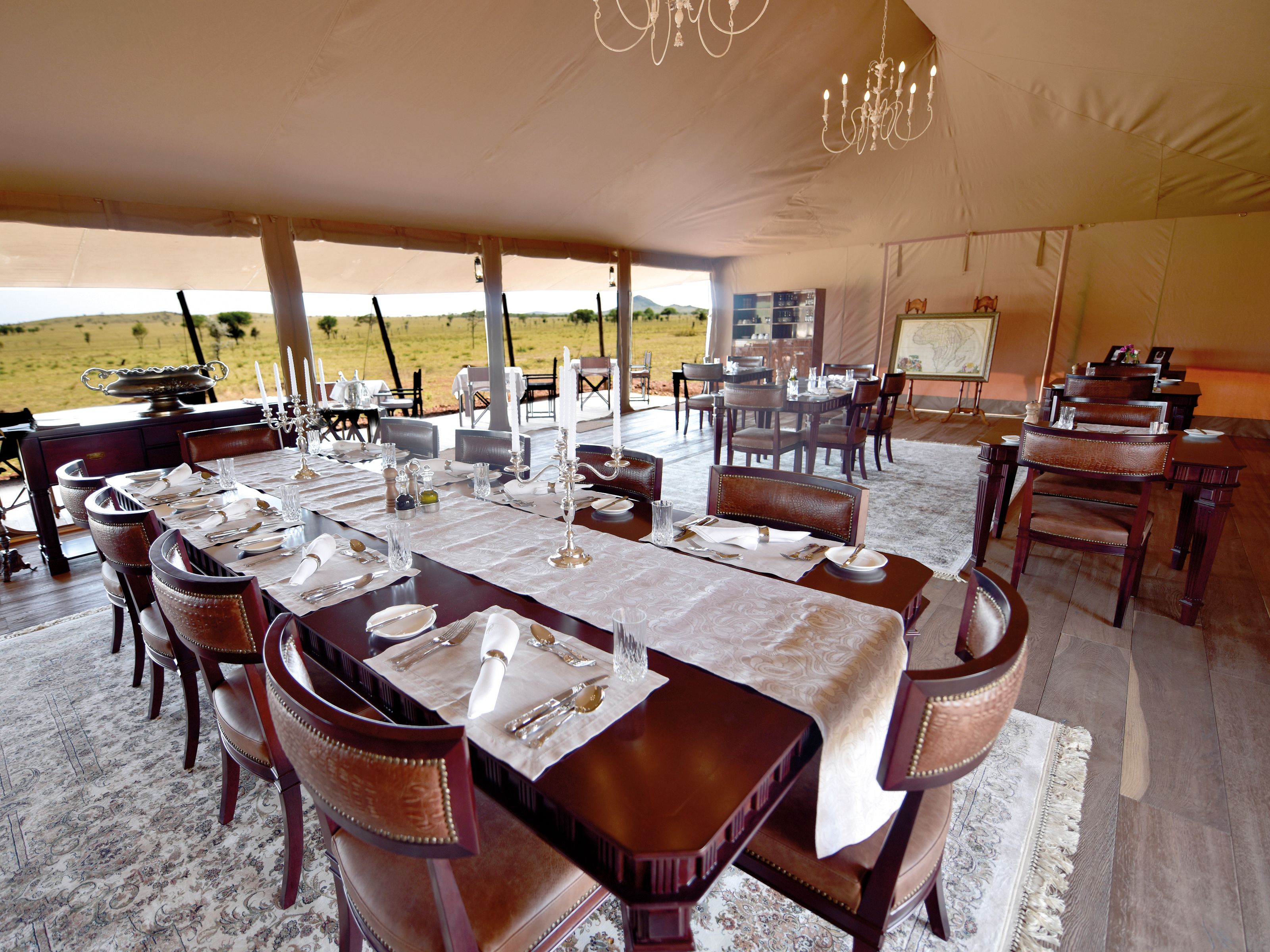 Un espace de restauration aménagé sous une tente, avec des tables dressées pour le repas, des chaises et un lustre.