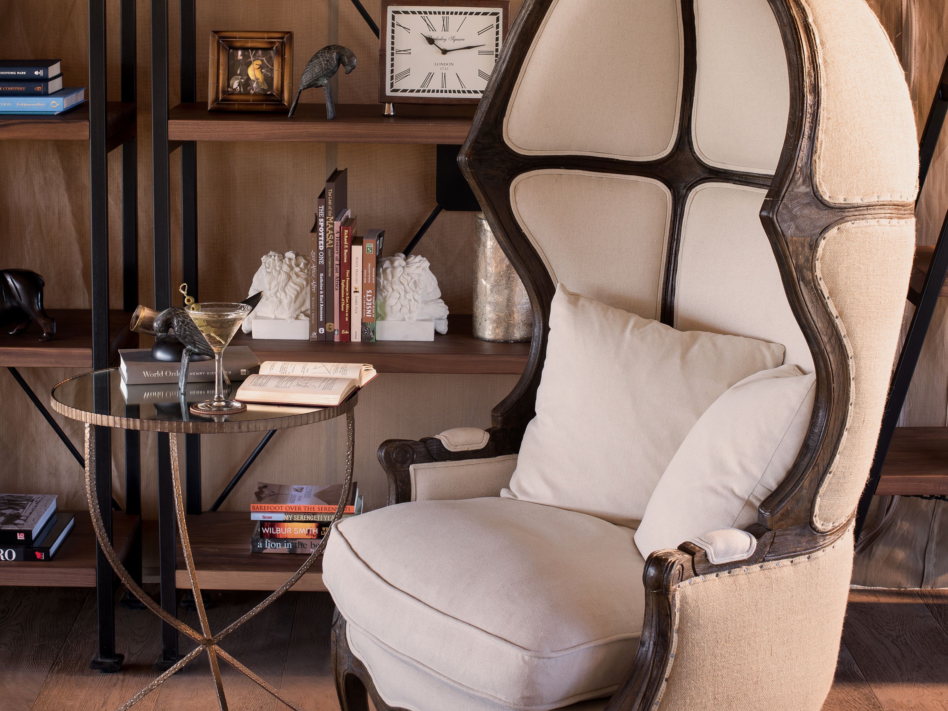 Una sala de estar moderna con un sillón de respaldo alto, una mesa de centro de vidrio y una estantería con libros y objetos decorativos.