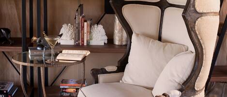 Una sala de estar moderna con un sillón de respaldo alto, una mesa de centro de vidrio y una estantería con libros y objetos decorativos.