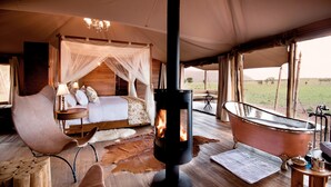 A tented room with a bed, a sitting area, a wood-burning stove, and a bathtub.