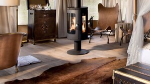 A cozy room with a wood-burning stove, leather furniture, and a large window with curtains.