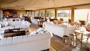 A tented accommodation with a lounge area featuring sofas, a bar, and a view of the outdoors.