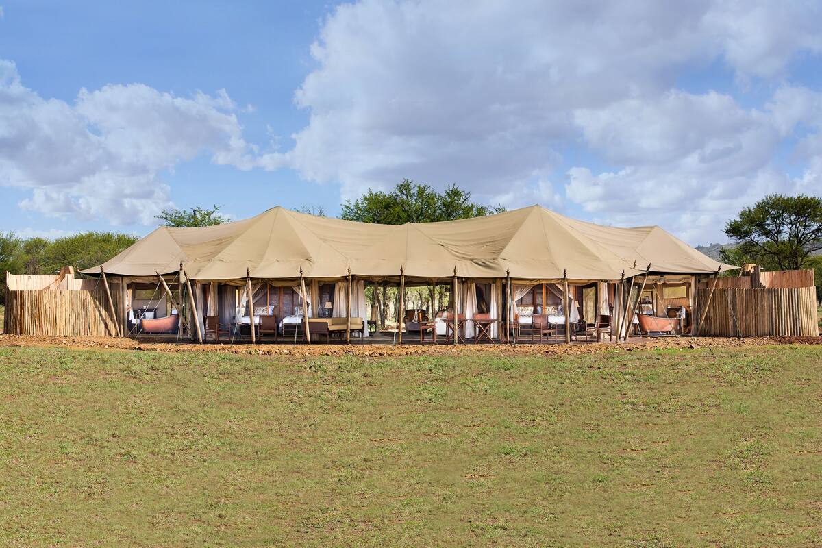 A safari tent with multiple rooms, each with a bed and a table.