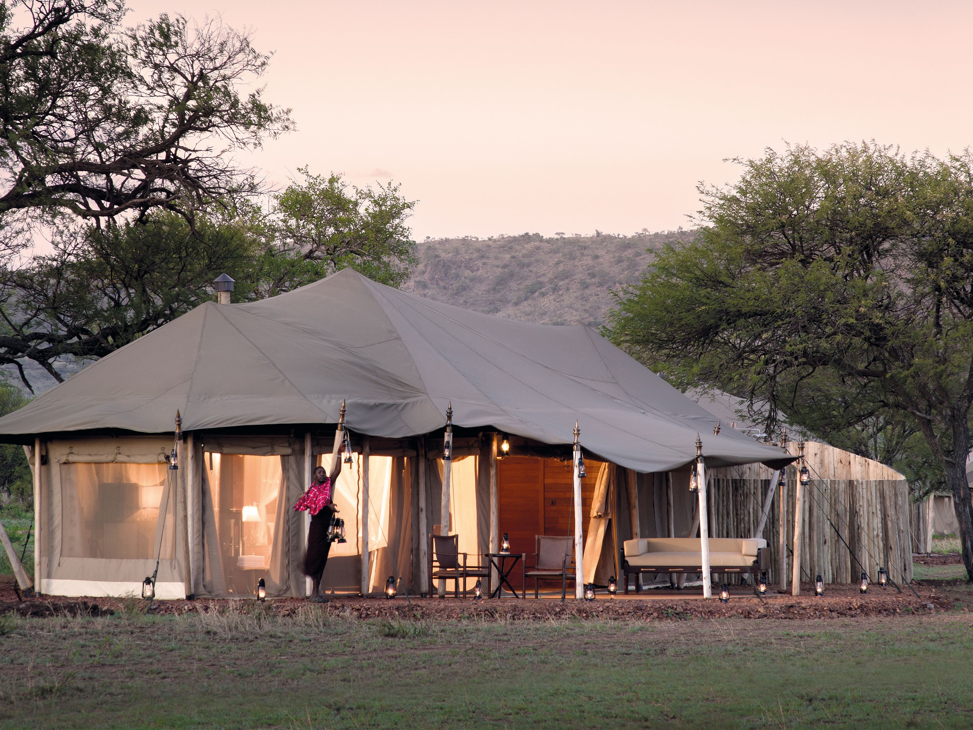 Een grote tent met een overdekte veranda, houten meubels en lantaarns.