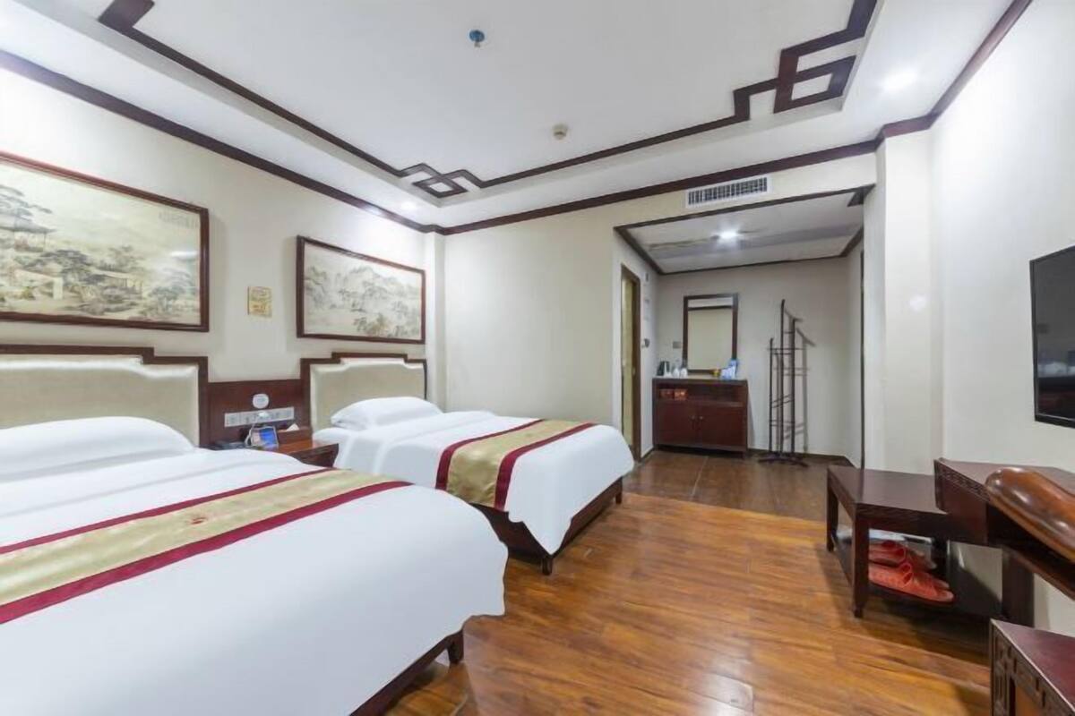 A hotel room with two beds, wooden flooring, a desk, and a television.