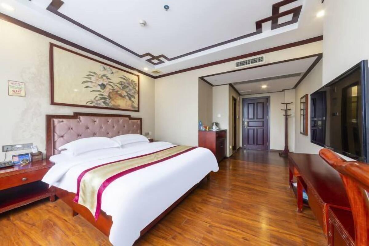 A hotel room with a large bed, wooden flooring, a television, and a painting on the wall.