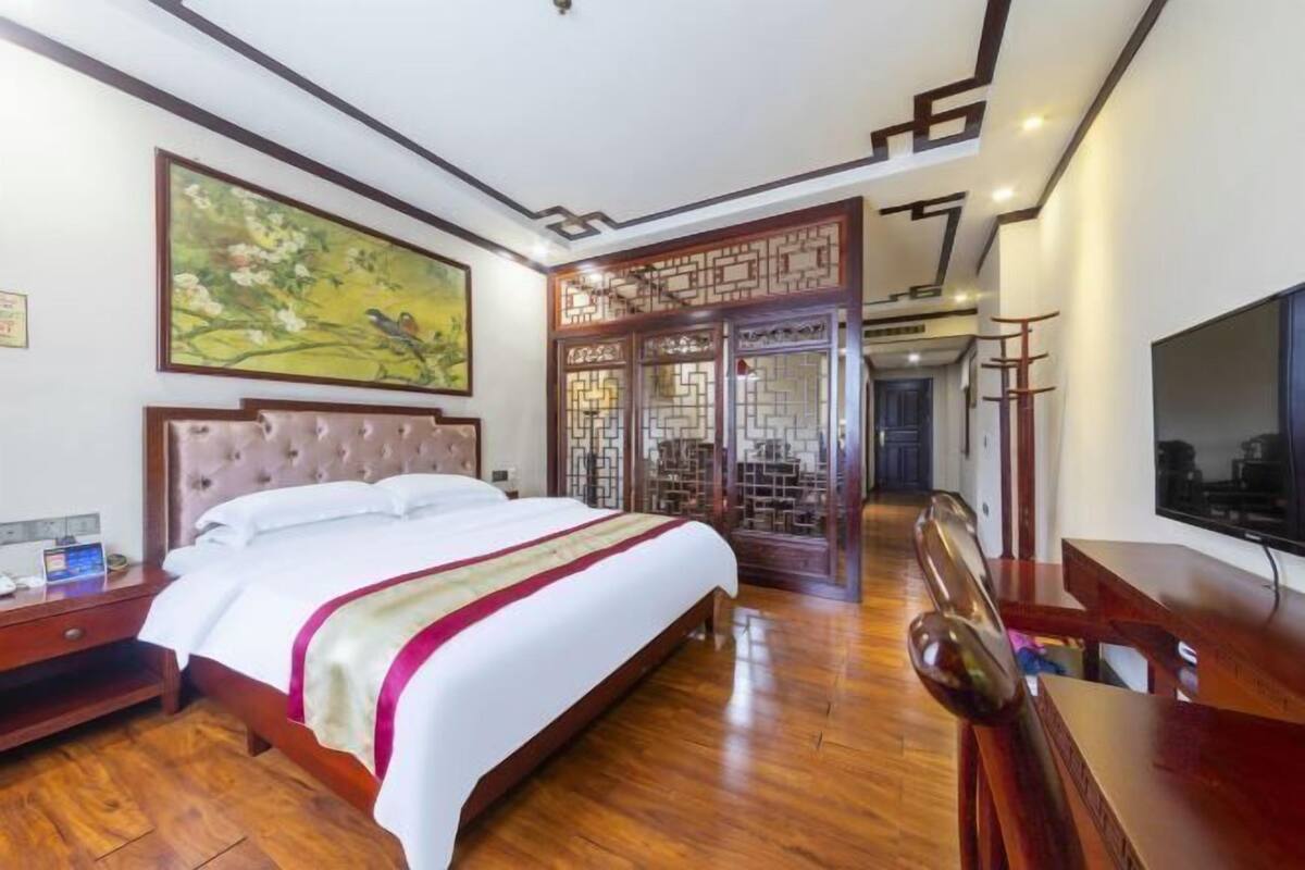 A hotel room with a large bed, wooden flooring, a TV, a desk, and a decorative screen.