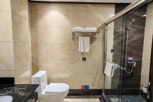 A modern bathroom with a toilet, a glass-enclosed shower, and a marble-tiled wall.