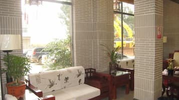 A room with a sofa, a table, and a chair, a lamp, and a potted plant.