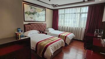 A hotel room with two beds, a large window with curtains, a painting on the wall, and a desk with a chair.