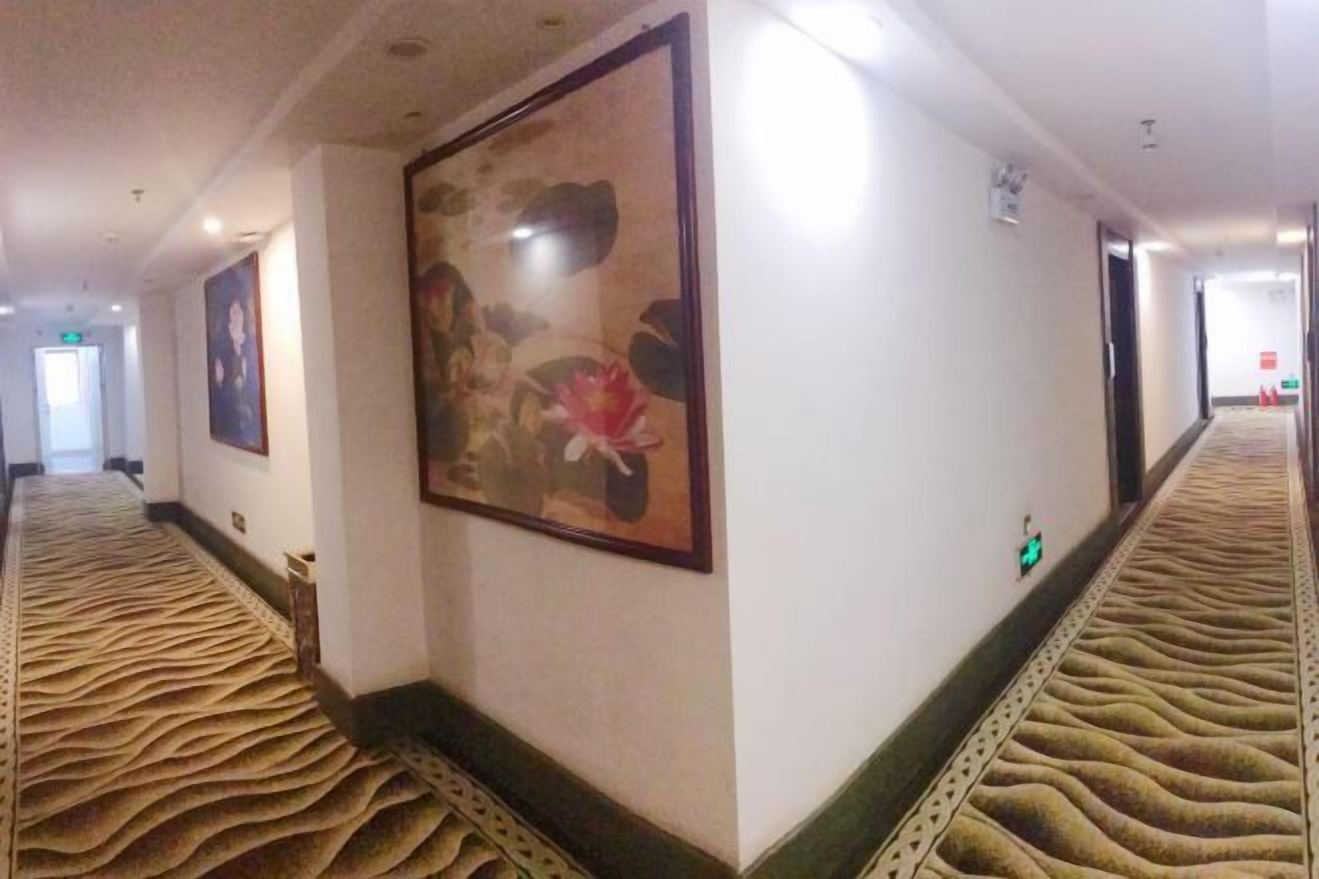 Un pasillo de hotel con alfombra estampada, cuadros enmarcados en las paredes y puertas que dan a las habitaciones.