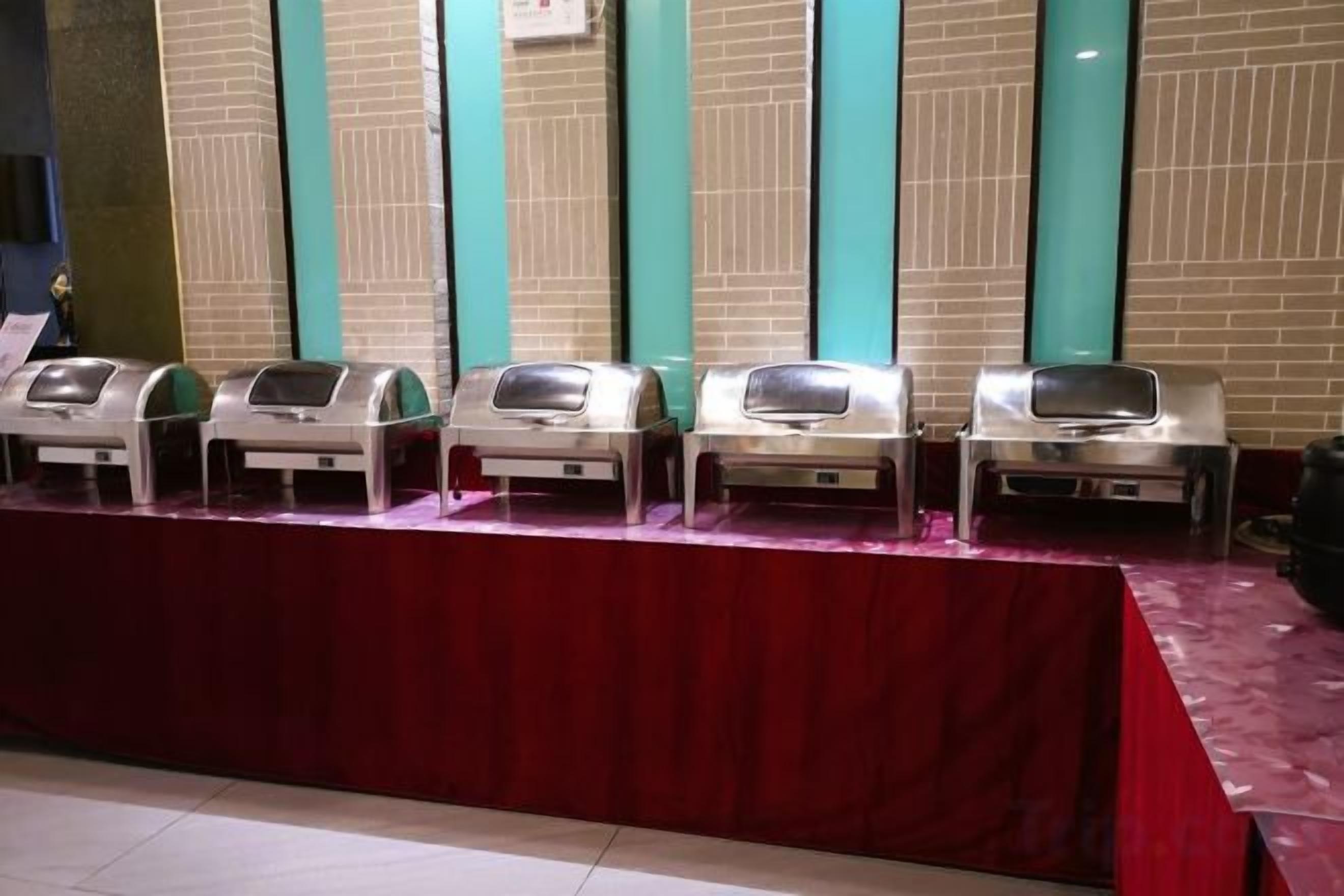 A row of buffet-style food dispensers on a table with a red tablecloth.