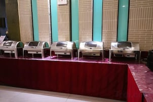 Una fila de dispensadores de comida tipo buffet sobre una mesa con mantel rojo.