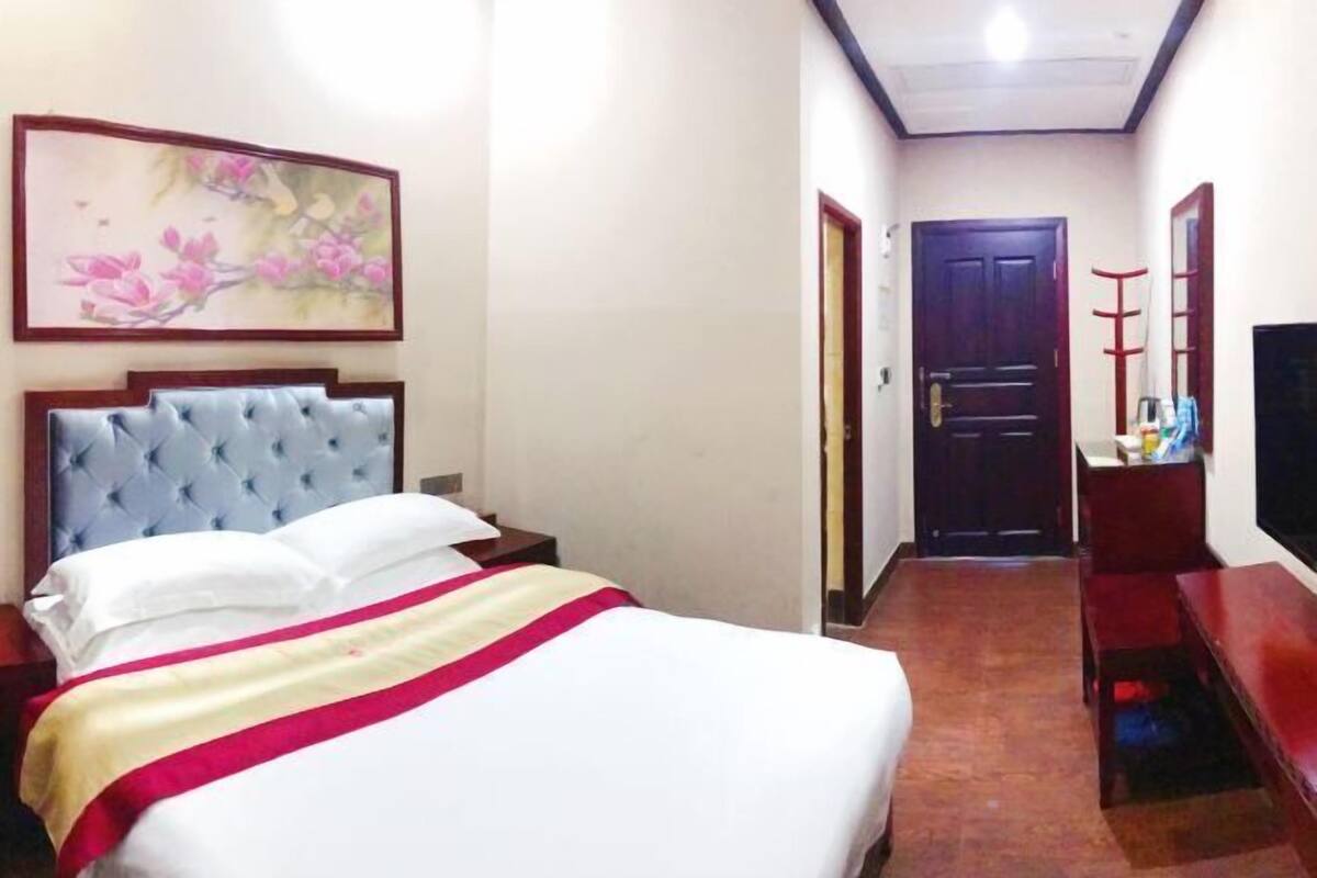 A hotel room with a bed, a painting, a wooden door, and a television.