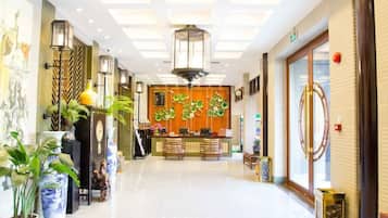 A hotel lobby with a reception desk, seating area, and decorative plants.