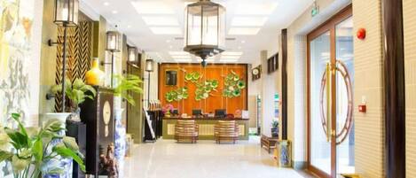 Un vestíbulo de hotel con mostrador de recepción, zona de estar y plantas decorativas.