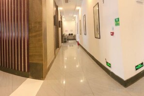 A hotel corridor with a wooden partition on the left, framed pictures on the walls, and emergency exit signs. - Heyuan Boutique Hotel (Shaoguan High-speed Railway Station) (Shaoguan)